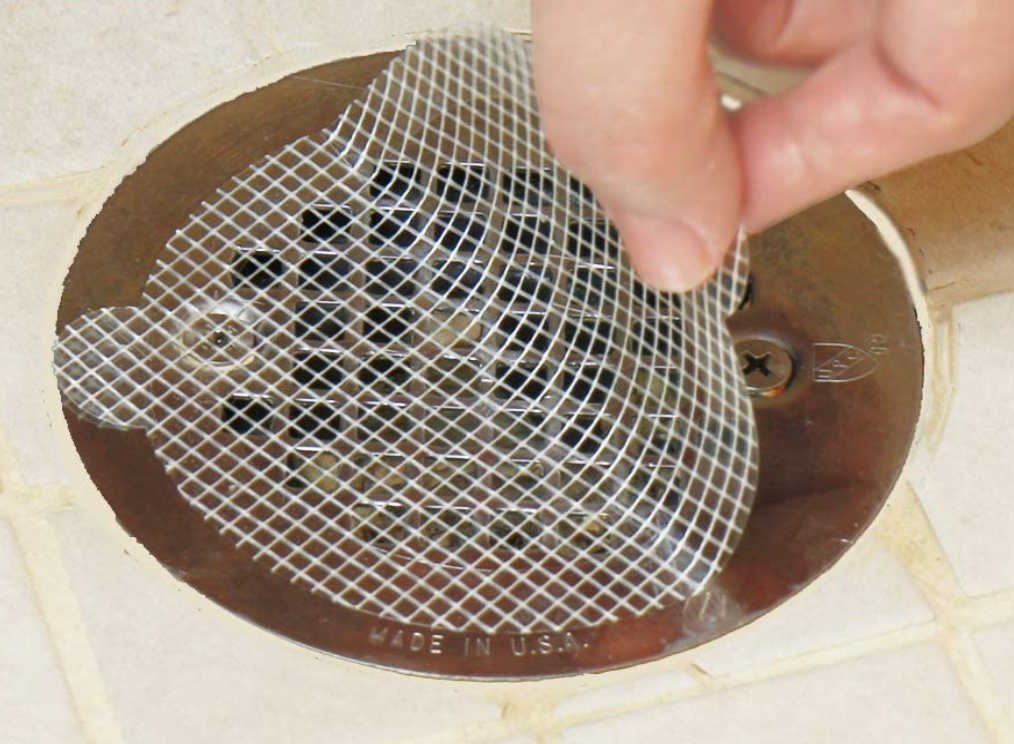 A small circular transparent sticker being placed over a flat shower drain