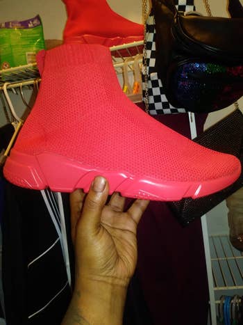 A manus holds a reddish knitted high-top sneaker, showcasing its sleek, modern plan successful a buying setting