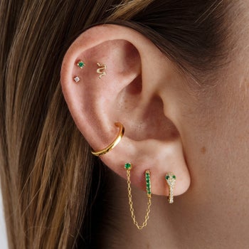 model wearing the snake huggie earrings styled with other gold and green earrings