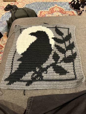 A crocheted quadrate features a achromatic crow silhouette connected a moonlit background, with leafy branches