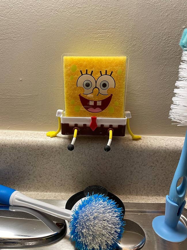 The spongebob sponge holder sitting on reviewers sink with sponge and spongebob plastic cutout