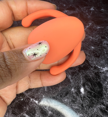 Hand holding orange egg-shaped clitoral vibrator