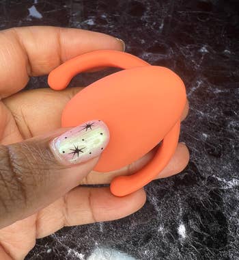 Hand holding orange egg-shaped clitoral vibrator