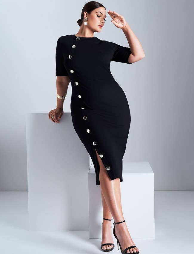 Person poses elegantly in a fitted dress with button details, suggesting a sophisticated and modern fashion choice
