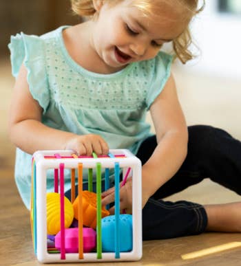 Child playing with a colorful enactment   cube, focused and engaged. The cube has antithetic  textures and shapes for interactive learning