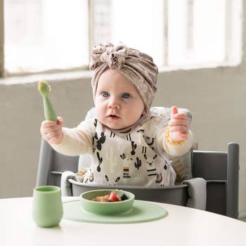 A baby eating with the green plate, glass, and spoon