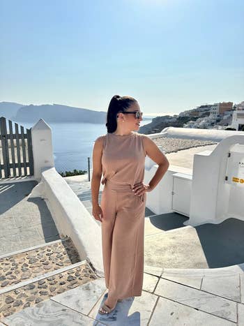 Person successful  a sleeveless jumpsuit and sunglasses stands outdoors, overlooking a coastal view