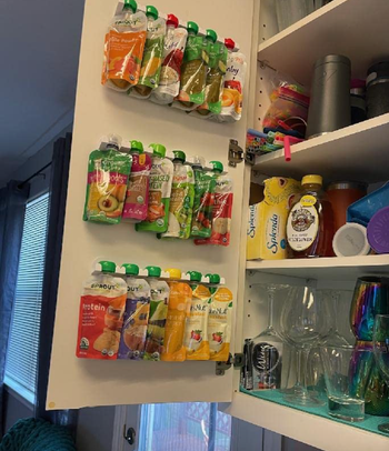 Snack pouches hanging from adhesive organizers on the inside of a cabinet 