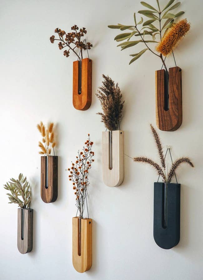 u-shaped wood vases with glass tube in between the wood holding plant stems. each is a different color and hang on the wall with string 