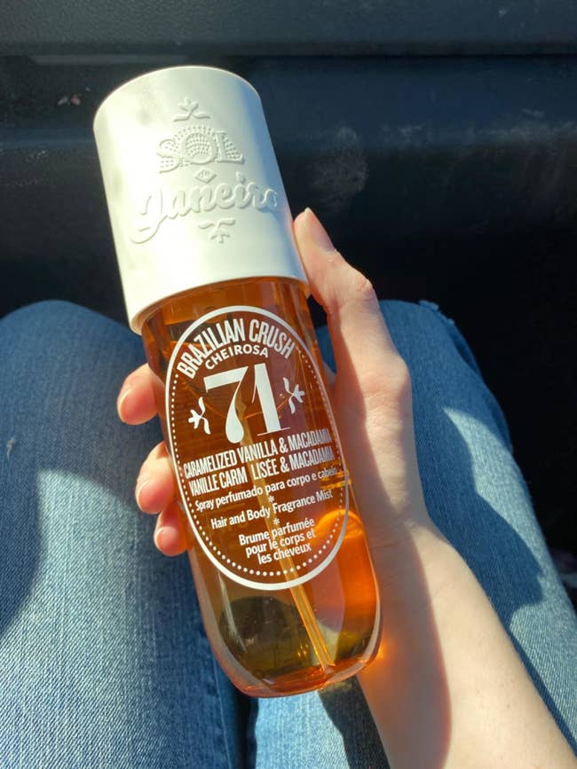 Hand holding Sol de Janeiro Cheirosa '71 assemblage spray vessel with achromatic cap, labeled for caramelized vanilla and macadamia scent
