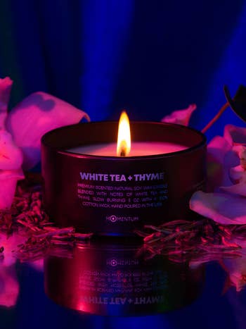 Black candle aflame surrounded by tea leaves and rose petals