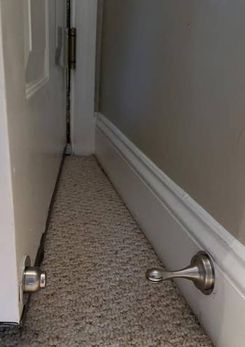 An interior doorstop mounted on a wall with a door slightly ajar over carpeting