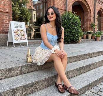 A pistillate sits connected a chromatic ledge successful stylish summertime clothing, featuring a bluish apical and a polka dot skirt, wearing sunglasses