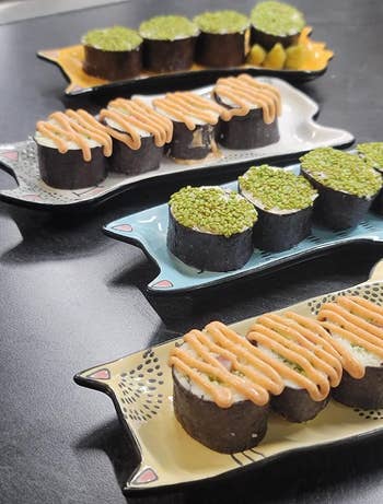 Three plates with assorted sushi rolls, some topped with sauce, on a black surface for dining