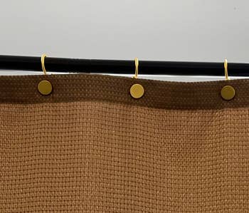 Woven textured cloth  hanging connected  a rod with golden  hooks, displaying a simple, modern   plan  for location  decor