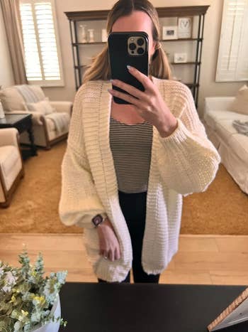 A reviewer taking a mirror selfie while wearing the cardigan in white