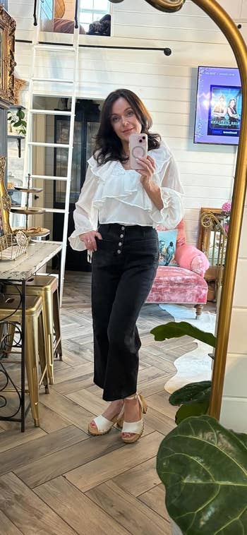 Reviewer in a ruffled white blouse and black jeans posing for a mirror selfie