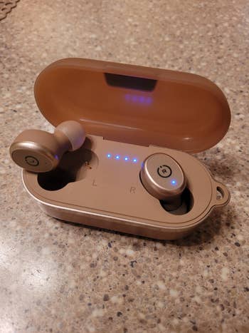 another reviewer's photo of one khaki earbud in the charging case and another sitting on top of it showing the silicone ear tip