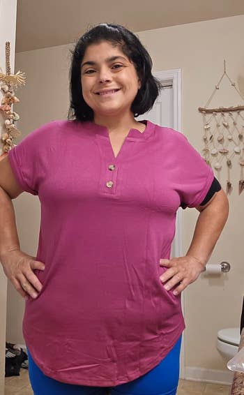 Person smiling, wearing a short-sleeve apical with fastener details successful a casual indoor setting