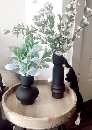 various florals arranged inside two of the black vases