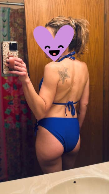 Woman in blue swimsuit taking a mirror selfie with a phone; tattoo visible on her back