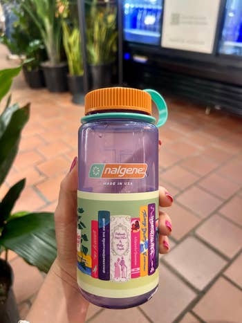 Hand holding a Nalgene vessel  with literary-themed stickers, displayed successful  a store   mounting  with plants successful  the background