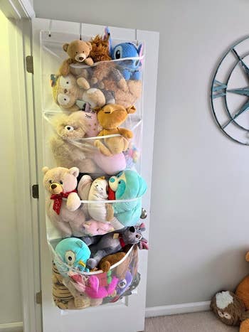 A achromatic doorway with hanging mesh organizers filled with assorted stuffed animals, including bears, unicorns, and characters similar Stitch and Olaf. A globe partition decoration is visible