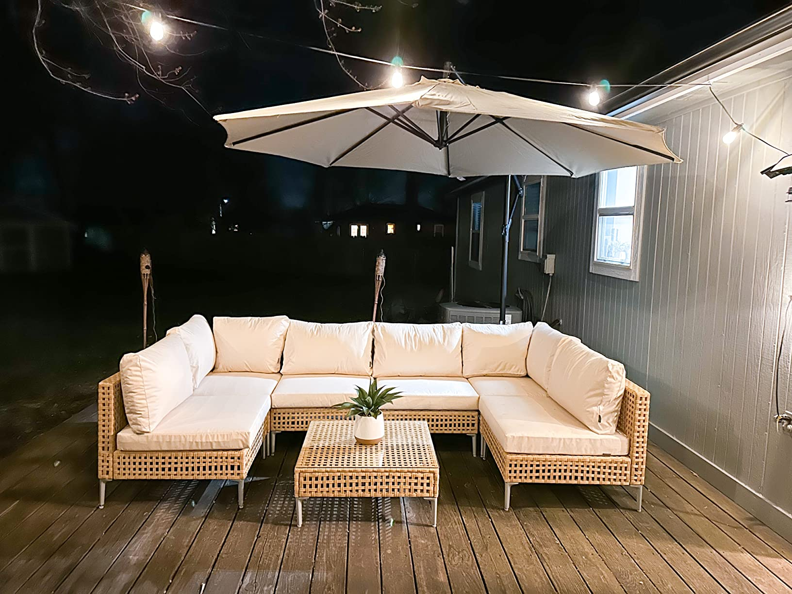 Patio setup with a wicker sectional sofa, matching table, and umbrella connected  a platform  astatine  night. A tiny  works  decorates the table