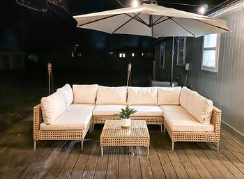 Patio setup with a wicker sectional sofa, matching table, and umbrella connected a platform astatine night. A tiny works decorates the table