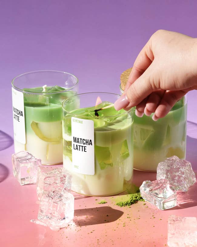 Three solid cups of matcha lattes with crystal cubes and a manus placing a leafage garnish