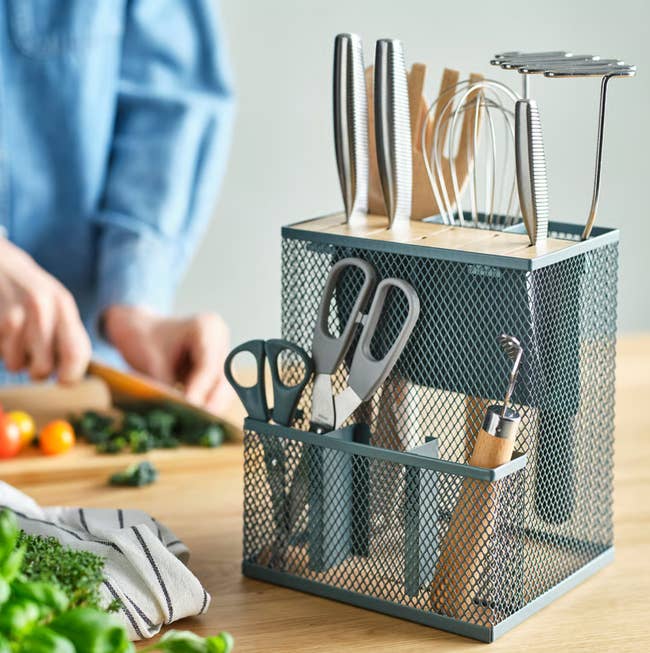 Person chopping vegetables with room  utensil holder successful  the foreground, containing knives, whisks, and scissors