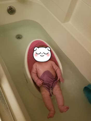 A baby in a tub of water while laying on the bath support