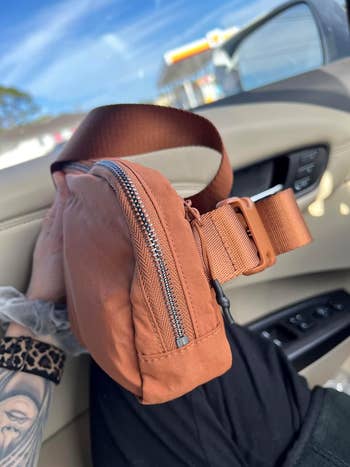 Reviewer holding a crossbody bag in a car, highlighting its zipper and adjustable strap