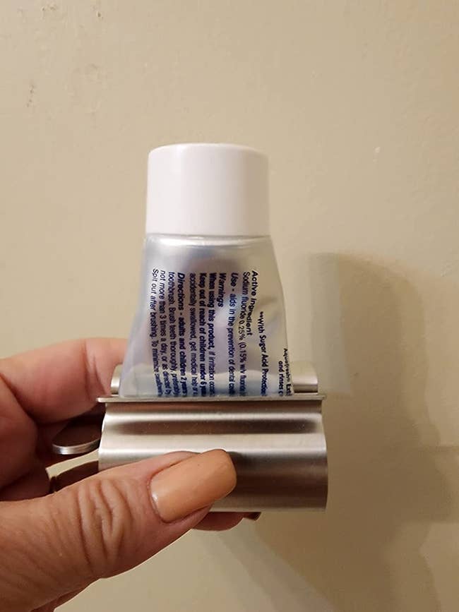 A reviewer holding their partially rolled toothpaste with the silver holder on the bottom