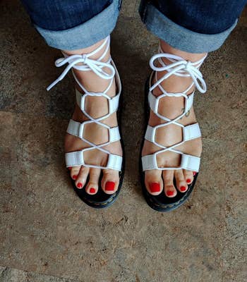 reviewer wearing white lace-up sandals and blue jeans, pedicure visible