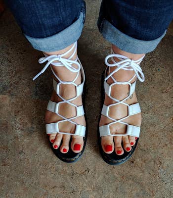 reviewer wearing white lace-up sandals and blue jeans, pedicure visible