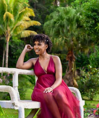 A reviewer wearing the dress in red while sitting on a bench