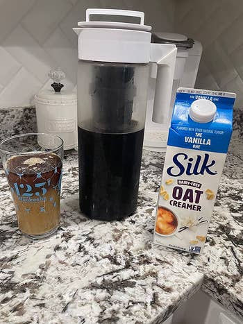 same cold brew maker with white lid next to cup of cold brew and silk oat milk creamer container