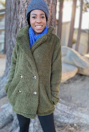 different reviewer wearing the green teddy coat buttoned up with a scarf