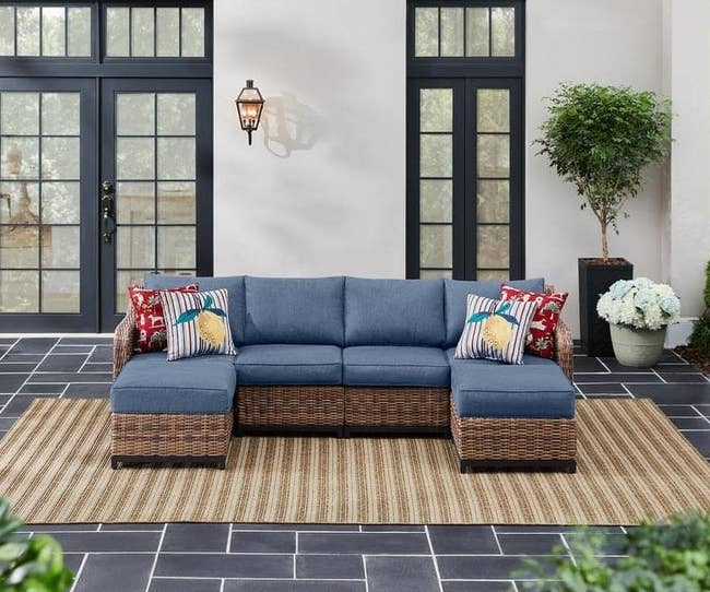 Outdoor setup with a blue wicker sectional sofa and patterned pillows on a patterned rug