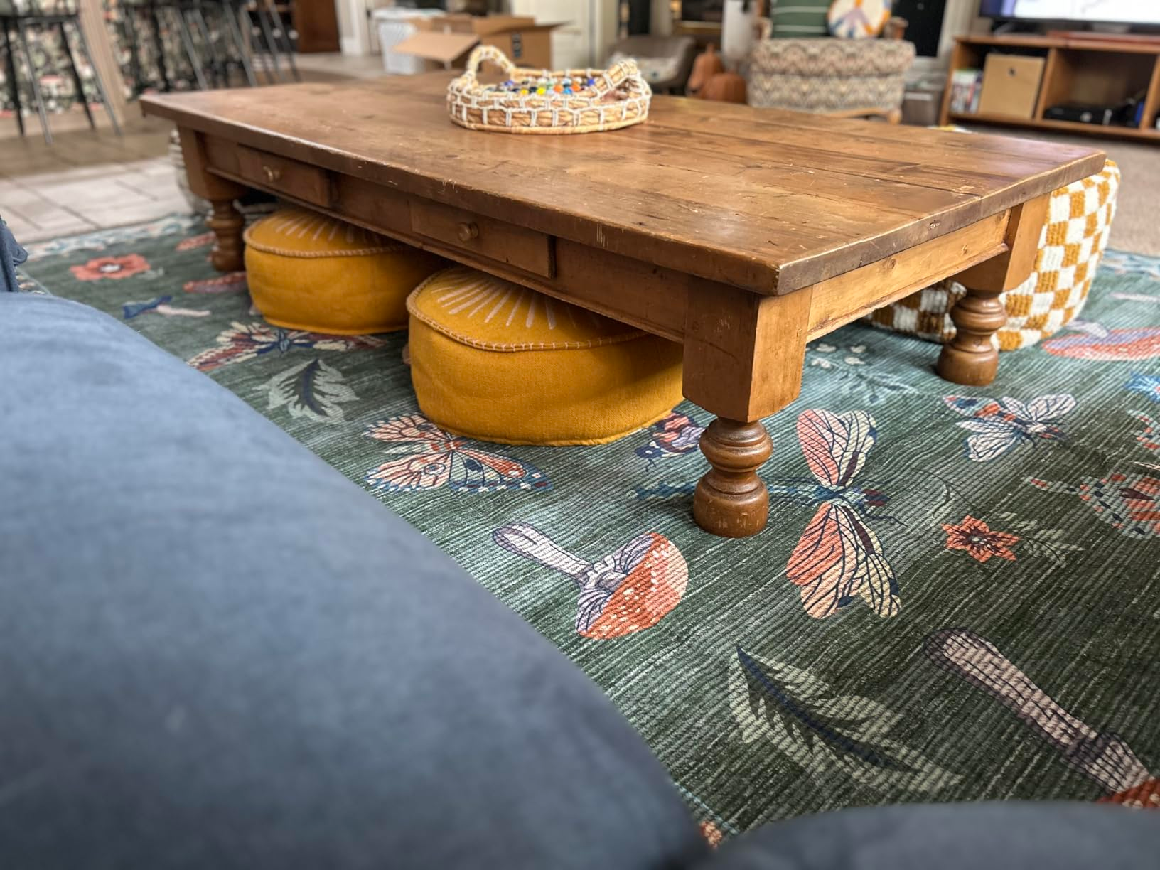 Coffee array  connected  floral rug with circular  cushions underneath, surrounded by cozy seating. Basket of decorative items connected  top. Cozy surviving  country   vibe