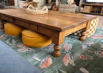 Coffee array connected floral rug with circular cushions underneath, surrounded by cozy seating. Basket of decorative items connected top. Cozy surviving country vibe