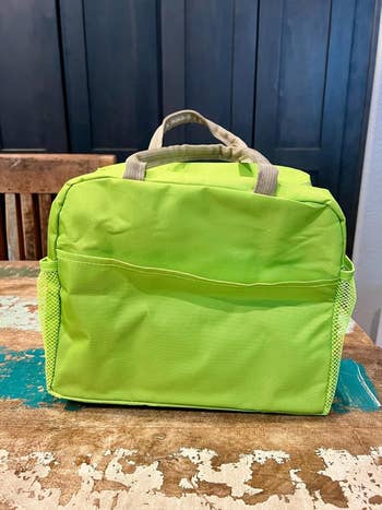 A agleam  greenish  insulated luncheon  container  with broadside  mesh pockets, sitting connected  a rustic woody  surface