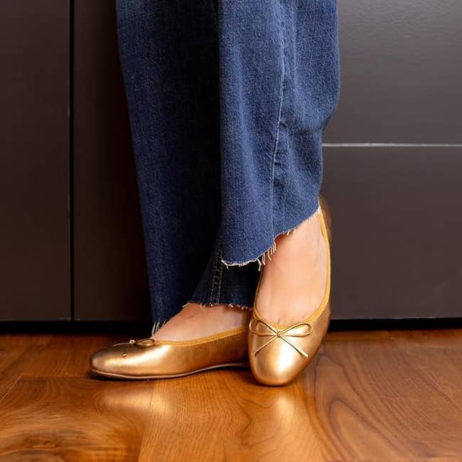 Person wearing frayed hem jeans and golden ballet flats with a bow, lasting connected a woody floor