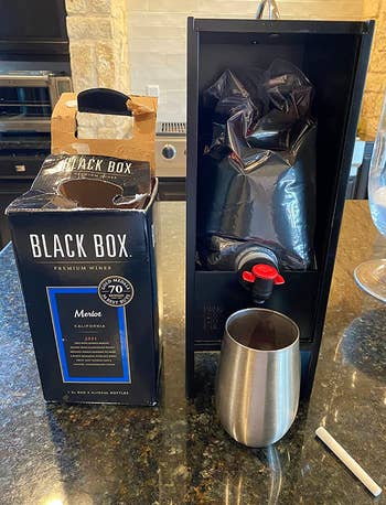 A black rectangular dispenser open on a counter to show the wine bag inside of it 