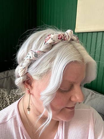 A reviewer with platinum blonde hair wears a floral scarf braided into their updo. 