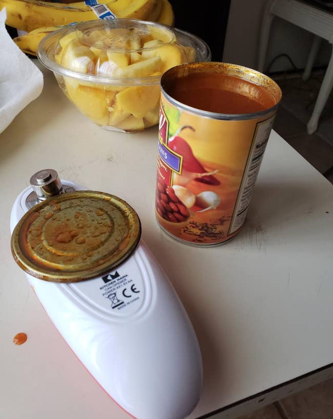A reviewer's small electric can opener with an open can lid attached to it 