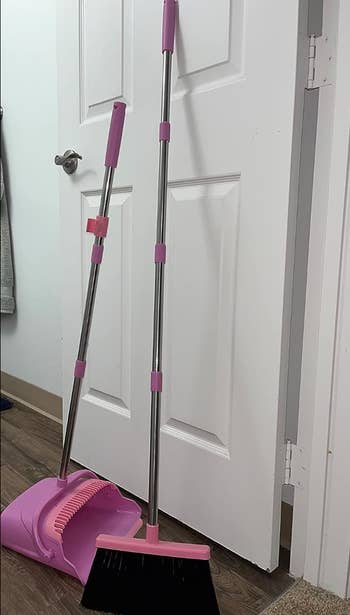 the pink broom and dust bin propped up against a wall 