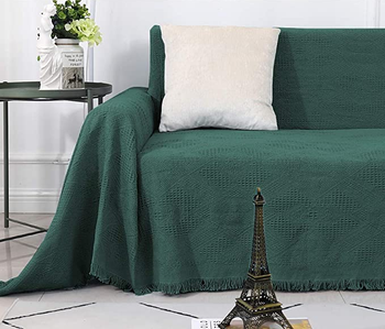 part of a sofa with a green throw cover on it and a white throw pillow