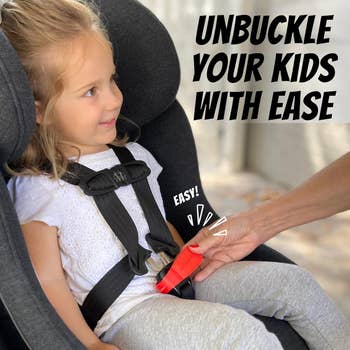 Child in car seat with adult hand demonstrating easy buckle release